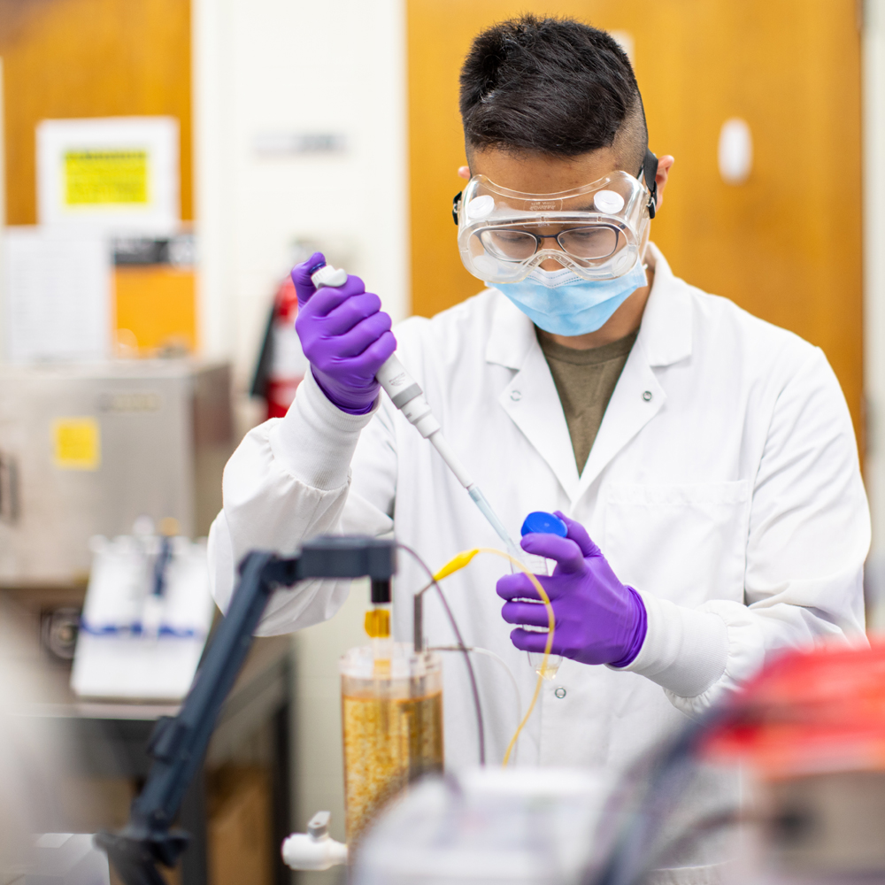 一个戴着护目镜和手套的学生在实验室里摆弄试管