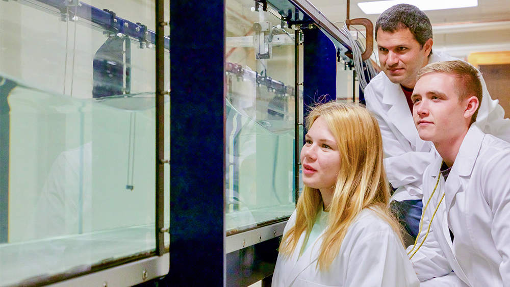 一位教授和两个学生在实验室里观察波浪箱模拟。