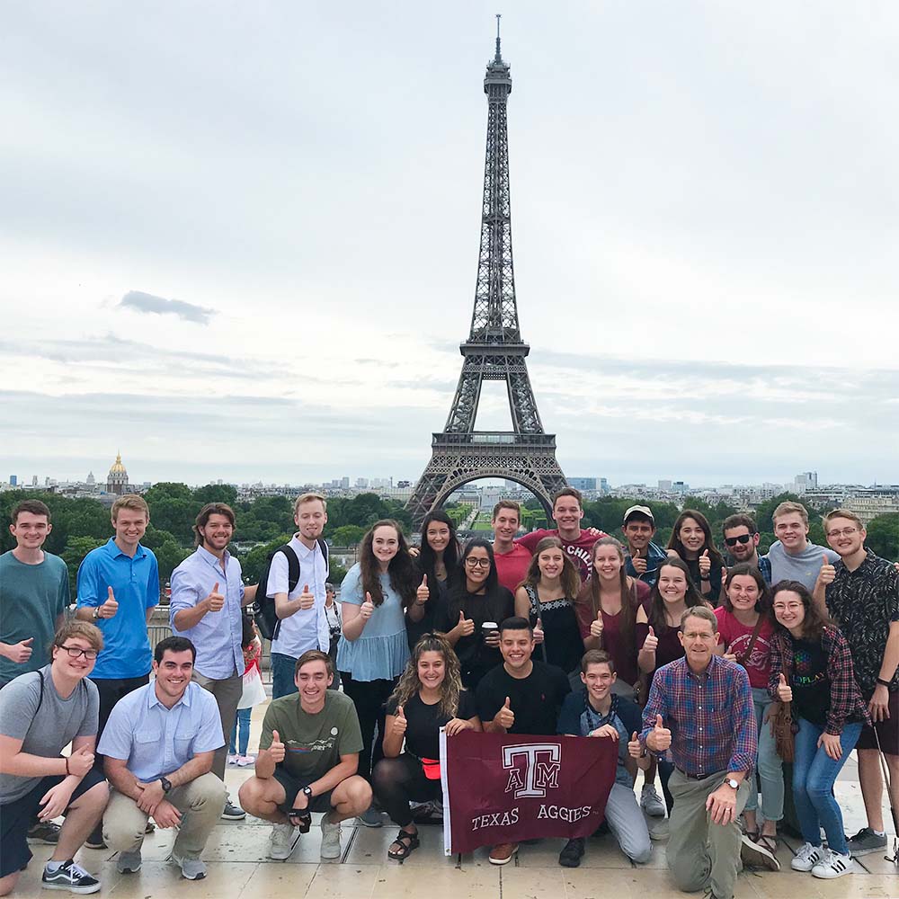 一大群留学生和教职工在埃菲尔铁塔前竖起大拇指，举着德州Aggies国旗。