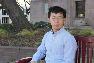Jun Oh坐在位于德州农工大学校园的户外木凳上