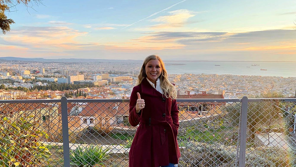 劳伦·威廉姆斯(Lauren Williams)站在俯瞰这座不断扩张的城市的美景前。她穿着一件栗色的外套，举着一个手势。