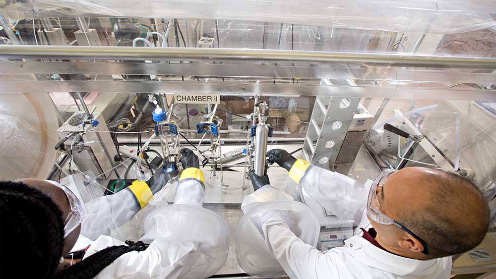 男女研究人员在封闭的实验站工作时穿着实验服和其他安全装备