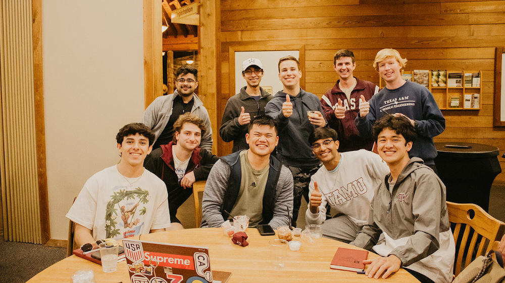 一群男学生围在一张桌子边微笑着摆姿势拍照。